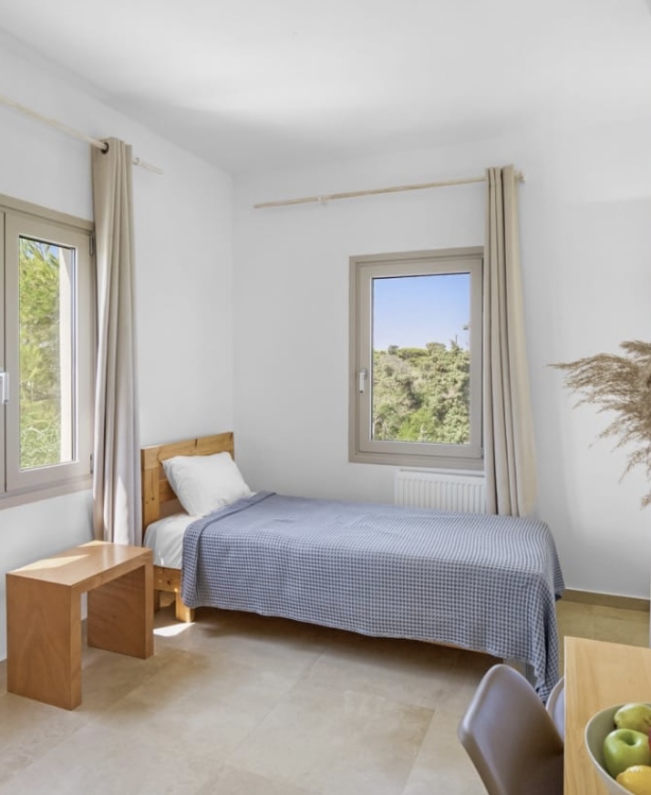 Single bed room with two windows over the greenery