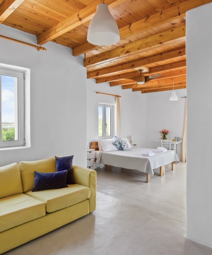Open studio with yellow sofa, windows and double bed beyond