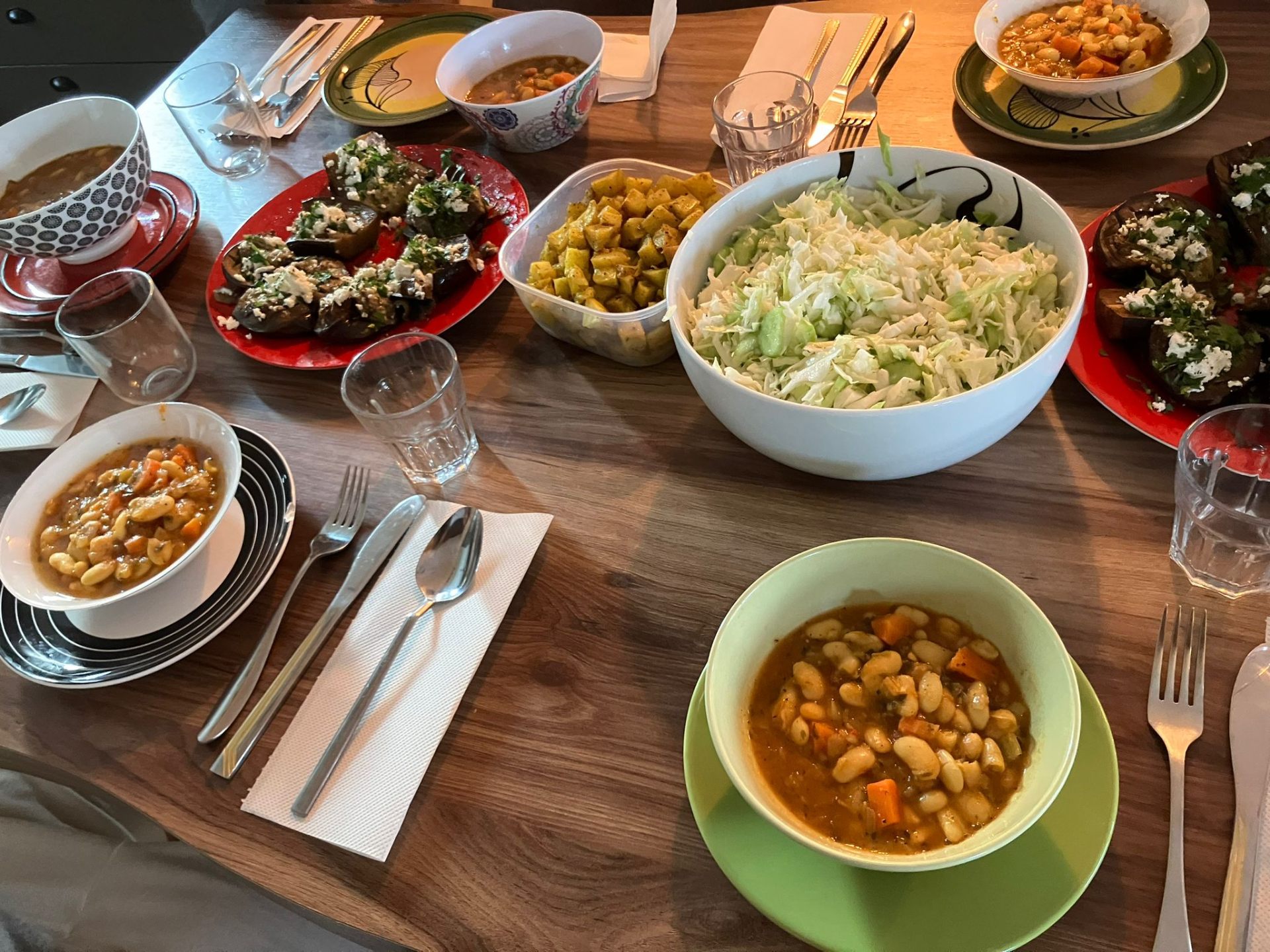 Shared table spread with bean stew, eggplant, salad and roasted potatoes