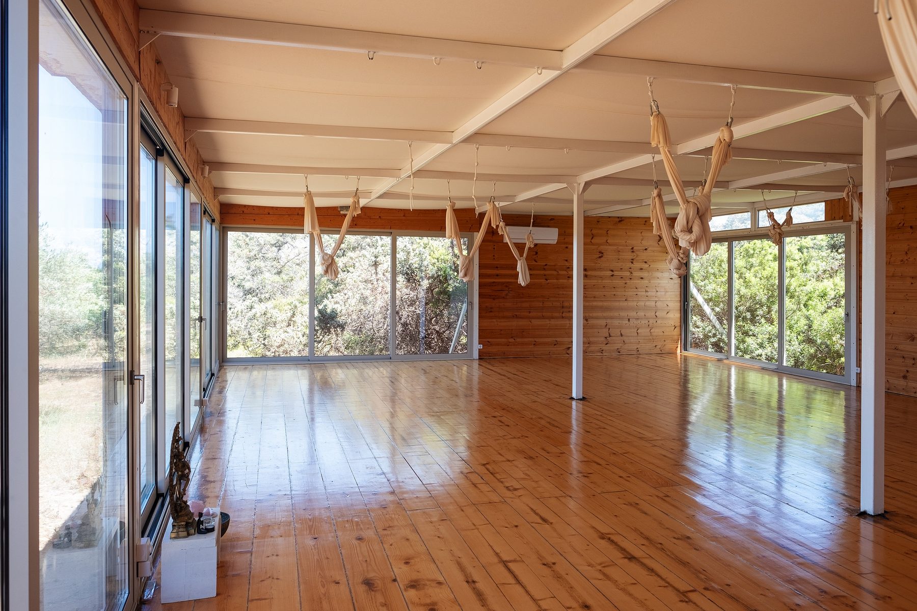 Shala interior with wooden floors, glass walls, and aerial hammocks