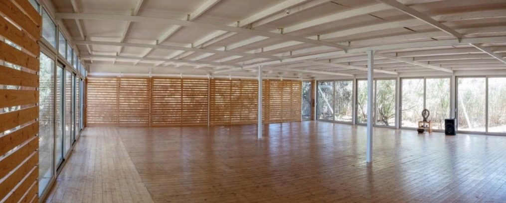 Wide empty shala with wooden floors and floor-to-ceiling glass walls